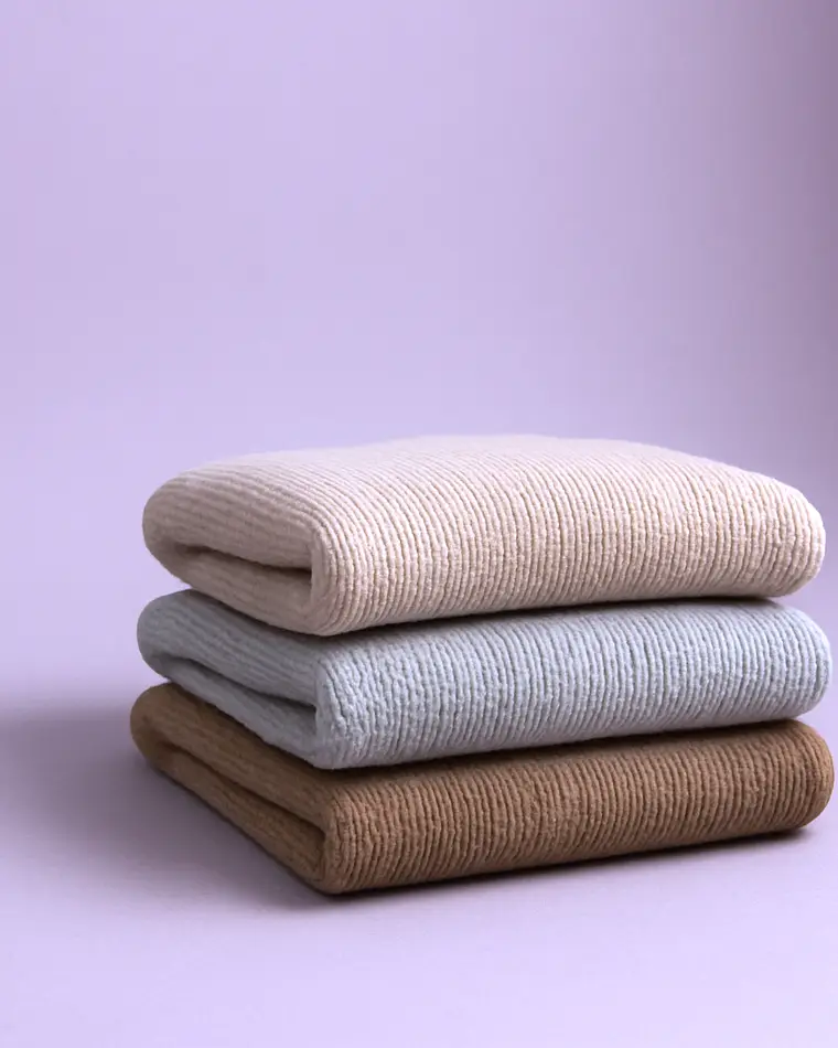 Three folded knit sweaters stacked on lilac paper.